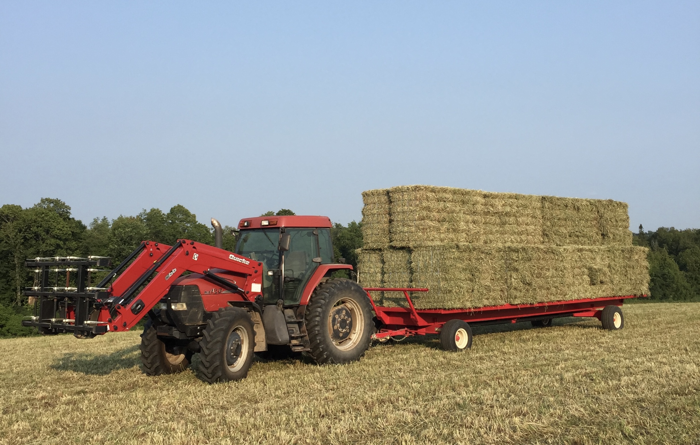 Red tractor pulling a wagon stacked with hay bundles in a harvested field
